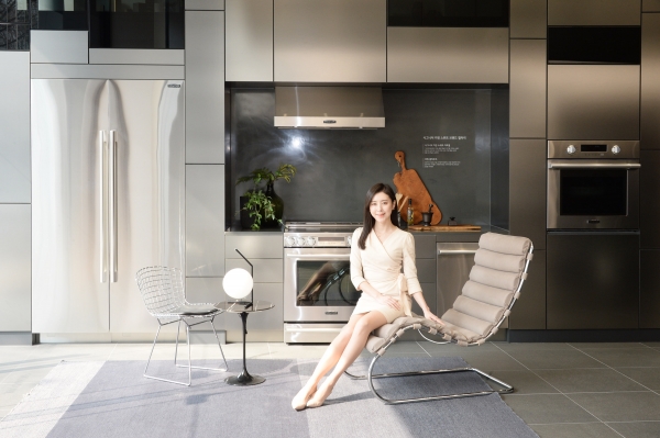 LG 모델이 놀의 제품 중 엠알 체어에 앉아 가전과 가구가 조화를 이루는 주방 공간을 소개하고 있다.